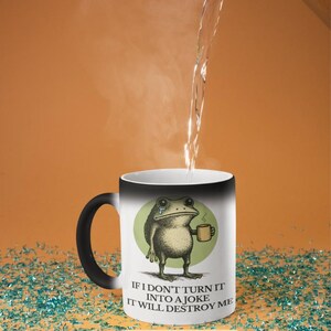 Puede incluir: Una taza m&aacute;gica que cambia de color con asa y borde negros. La taza presenta una rana llorando sosteniendo una taza, con el texto "IF I DON'T TURN IT INTO A JOKE IT WILL DESTROY ME". La taza es blanca y cambia de color.