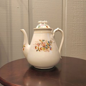May include: White porcelain teapot with a floral design featuring pink roses, green leaves, and red berries. The teapot has a white lid with a gold trim.
