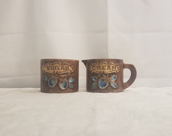 Könnte beinhalten: Ein Set aus zwei braunen Keramikbehältern für Zucker und Sahne mit einem Erdbeerdesign und den Worten "Zucker" und "Sahne" auf der Vorderseite.