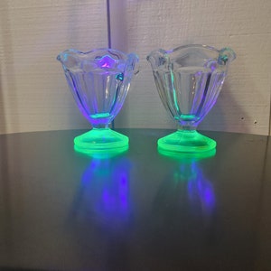 Op de afbeelding: Twee heldere glazen dessertschaaltjes met gegolfde randen en een voet. De voetjes zijn felgroen van kleur en de schaaltjes reflecteren een paars en groen licht.