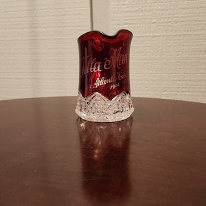 May include: A red glass pitcher with a clear glass base and a white design. The pitcher has the words "Jilla & Max" and "Atlantic City 1960" etched on the side.