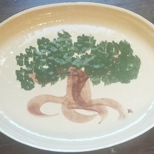 Puede incluir: Plato ovalado de cerámica con un diseño de árbol pintado a mano. El árbol presenta un tronco y raíces marrones, con un dosel de hojas verdes. El borde tiene un borde marrón claro. Una pieza única para servir.