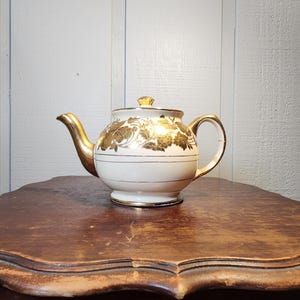 Könnte beinhalten: Eine weiße Keramiktasse mit schwarzem Henkel und dem Text "But first, coffee" in handschriftlichem Stil. Die Tasse steht auf einer weißen Oberfläche. Die Tasse ist 10 cm hoch.