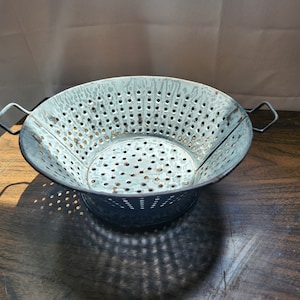 May include: A vintage blue metal colander with two handles. The colander is round and made of perforated metal.
