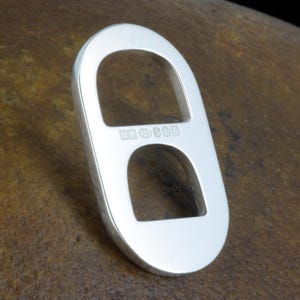 May include: A polished silver oval-shaped object with two open cutouts. The center bar features stamped hallmarks including the letters MP, the number 925, and three small symbols, indicating sterling silver composition and origin.