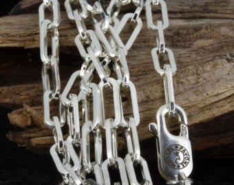 May include: A close-up of a silver chain necklace with rectangular links. The necklace has a lobster clasp closure. The background is a piece of wood.