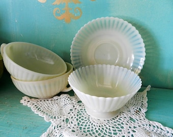 Può includere: Un set di quattro tazze da tè e piattini opalescenti bianchi con un design a coste. Le tazze e i piattini sono impilati uno sopra l'altro.