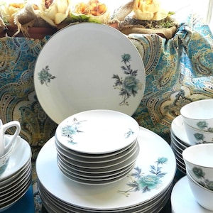 Könnte beinhalten: Ein Set weißer Porzellangeschirrs mit einem Blumendesign mit blauen und grünen Blumen. Das Set enthält Teller, Schalen und Tassen.