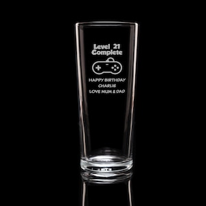 Op de afbeelding: Een helder glas met de tekst "Level 21 Complete" en een controller-afbeelding. Daaronder staat "Happy Birthday Charlie Love Mum & Dad". Het glas is hoog en cilindrisch.
