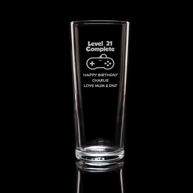 Op de afbeelding: Een helder glas met de tekst "Level 21 Complete" en een controller-afbeelding. Daaronder staat "Happy Birthday Charlie Love Mum & Dad". Het glas is hoog en cilindrisch.