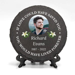Può includere: Una targa commemorativa in ardesia nera con un bordo bianco e una foto di un uomo. La targa recita "Se l'amore ti avesse potuto salvare, avresti vissuto per sempre. Richard Evans 1987-2022".
