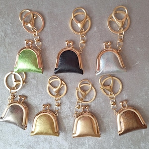 Puede incluir: Una colección de llaveros con pequeños dijes en forma de monedero en varios colores metálicos, incluyendo oro, plata y bronce. Cada llavero tiene un cierre y un anillo de color dorado.