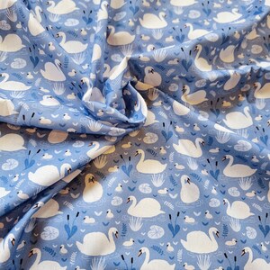 Pu&ograve; includere: Tessuto blu con un motivo di cigni bianchi. I cigni nuotano in uno stagno con ninfee e canne. Il tessuto &egrave; perfetto per il quilting, la cucitura e l'artigianato.