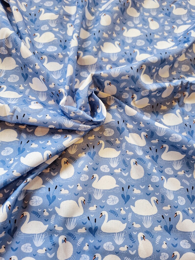 Pu&ograve; includere: Tessuto blu con un motivo di cigni bianchi. I cigni nuotano in uno stagno con ninfee e canne. Il tessuto &egrave; perfetto per il quilting, la cucitura e l'artigianato.