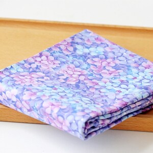 May include: A folded piece of fabric with a floral print in shades of purple, blue, and white. The fabric has a subtle shimmer.