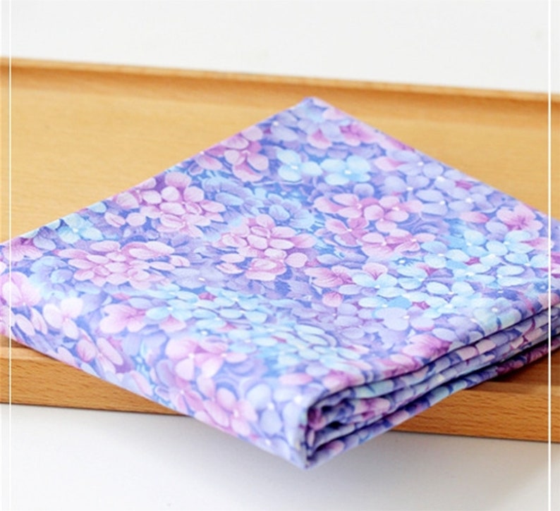 May include: A folded piece of fabric with a floral print in shades of purple, blue, and white. The fabric has a subtle shimmer.