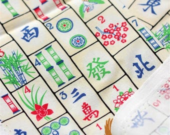 May include: A fabric textile featuring a repeating grid pattern of Mahjong tiles. The off-white background displays various colorful tile designs including green bamboo stalks, red floral motifs, blue Chinese characters, and circular patterns.