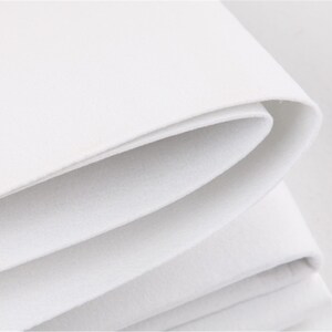 May include: Close-up of white felt fabric folded in layers, showing the soft texture and smooth surface.