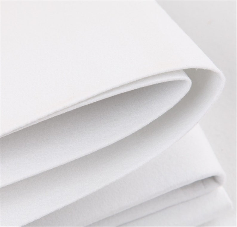 May include: Close-up of white felt fabric folded in layers, showing the soft texture and smooth surface.