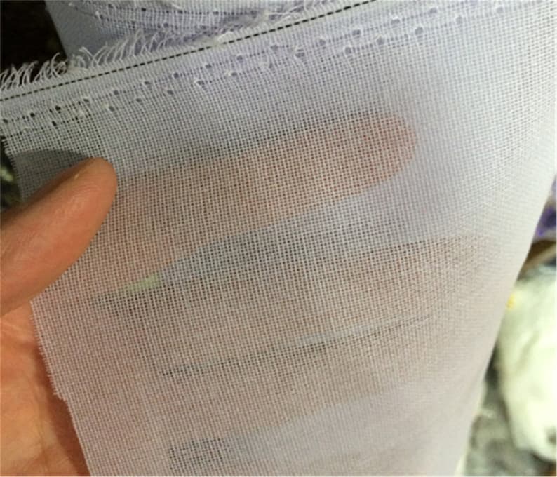 May include: White sheer fabric with a fine mesh weave. The fabric is folded and has a stitched edge.