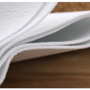 May include: Close-up of a white, folded fabric. The fabric is soft and textured, with a slightly fuzzy surface.