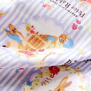 May include: A white fabric with a blue and white striped pattern. The fabric features a colorful illustration of Peter Rabbit and a teapot with flowers and text that reads "Beatrix Potter Peter Rabbit".