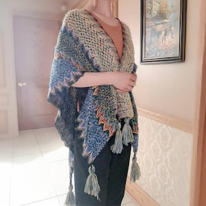 May include: A blue, green, and yellow crocheted shawl with fringe tassels. The shawl is draped over a person's shoulders.