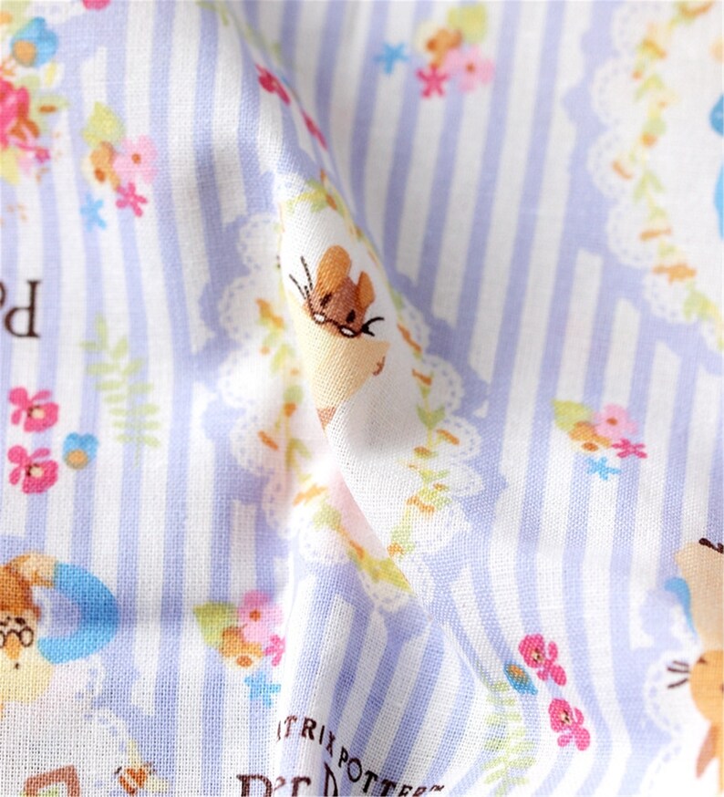 May include: A white fabric with a light blue and white striped pattern. The fabric features a repeating pattern of small flowers, leaves, and mice wearing glasses. The text " Beatrix Potter" is visible in the bottom right corner.