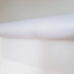 May include: A white roll of paper is mounted on a wooden dowel. The paper is unfurled and hanging down.