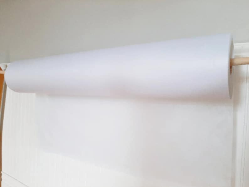May include: A white roll of paper is mounted on a wooden dowel. The paper is unfurled and hanging down.