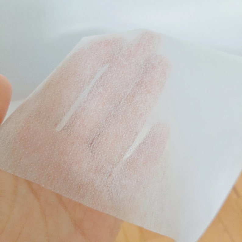 May include: A white, thin, textured sheet of fabric. The fabric is translucent and has a slightly rough texture.