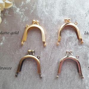 Puede incluir: Cuatro cierres metálicos para monederos en oro mate, oro claro, bronce y plata. Cada cierre tiene forma de arco redondeado con cierre de bola y pequeños bucles para sujetar a un bolso. El texto "Matte gold", "Light gold", "Bronze" y "Silver" es visible.