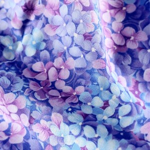 May include: A close-up of a fabric with a floral pattern. The fabric is a light blue color with purple and white flowers.