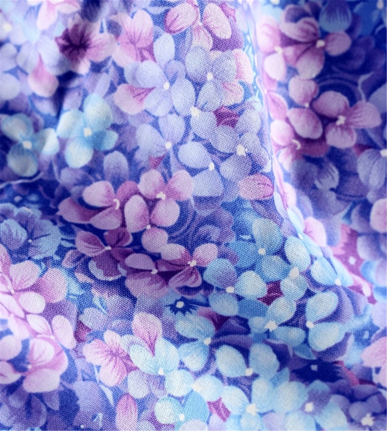 May include: A close-up of a fabric with a floral pattern. The fabric is a light blue color with purple and white flowers.