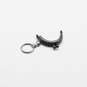 May include: A black metal purse frame with a key ring attached. The frame has a decorative pattern and two small round knobs.