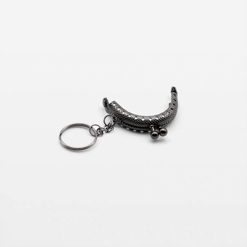 May include: A black metal purse frame with a key ring attached. The frame has a decorative pattern and two small round knobs.