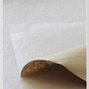 May include: A close-up of a white, textured, adhesive sheet with a brown paper backing. The backing is partially peeled back to reveal the adhesive.