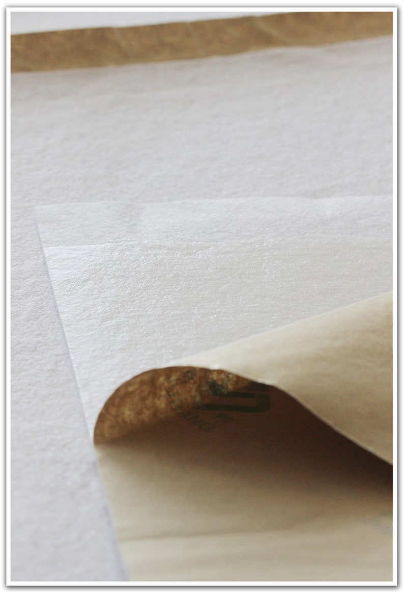 May include: A close-up of a white, textured, adhesive sheet with a brown paper backing. The backing is partially peeled back to reveal the adhesive.