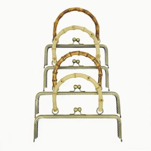 Puede incluir: Cuatro marcos de bolso con asas de bambú en tonos marrones y crema. Los marcos metálicos son de color bronce y las asas son arqueadas. Los marcos están apilados, mostrando los diferentes colores y estilos de las asas.