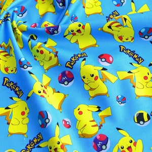 May include: Light blue fabric with a repeating pattern of yellow Pikachu characters, red and white Pok&eacute; Balls, and the word "Pok&eacute;mon" in white. Ideal for crafting projects, the fabric has a playful design.