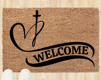May include: A brown coir doormat with the words "Welcome" in a black cursive font. A black heart with a cross on top is above the word "Welcome".