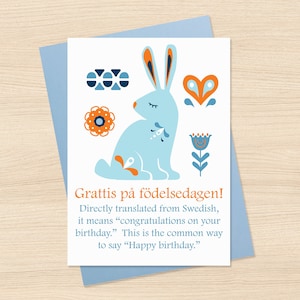 May include: A light blue birthday card with a stylized illustration of a rabbit and floral elements in orange and blue. The card reads "Grattis på födelsedagen!" which means "Happy birthday."