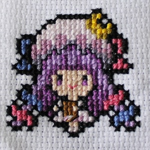 Könnte beinhalten: Kreuzstichmuster eines Zeichentrickcharakters mit lila Haaren, einem gelben Halbmond und einem braunen Outfit. Die Figur ist von schwarzen Stichen umgeben und vor einem weißen Stoffhintergrund platziert. Das Design verwendet verschiedene Lila-, Rosa- und Blautöne.