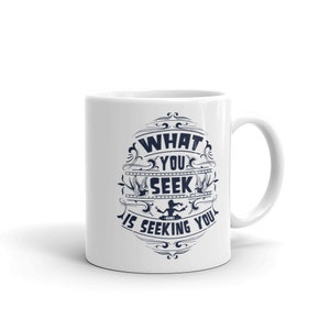 May include: White ceramic coffee mug with a blue design that says "What you seek is seeking you".