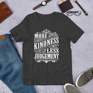May include: Dark heather grey t-shirt with a white graphic design that reads "More Kindness Less Judgement" in a vintage style font.