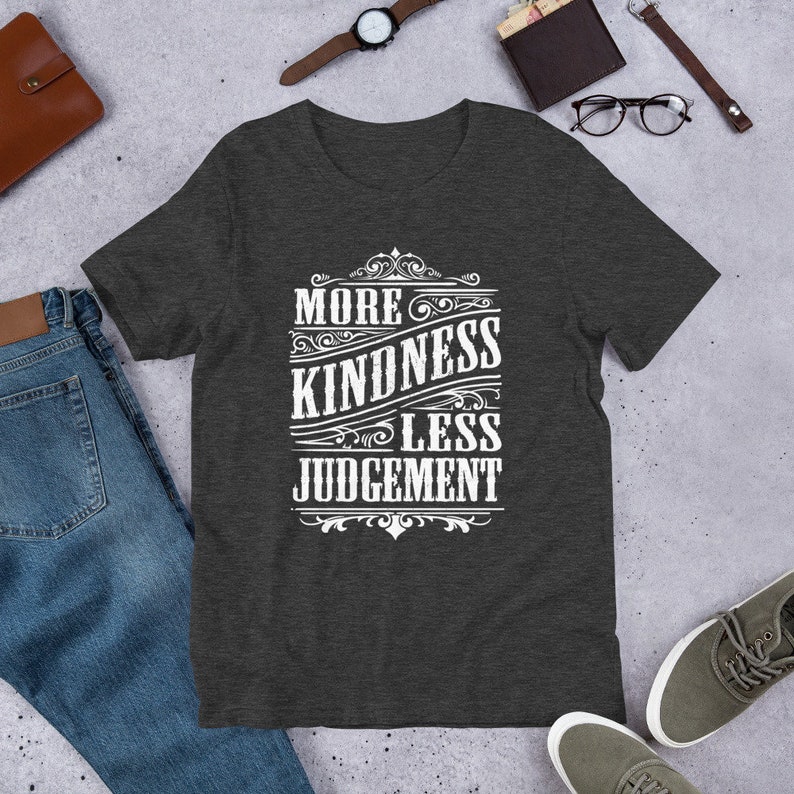 May include: Dark heather grey t-shirt with a white graphic design that reads "More Kindness Less Judgement" in a vintage style font.