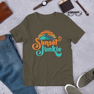 May include: A dark green t-shirt with a retro-style graphic of a mountain range with a sunset behind it. The text "Sunset Junkie" is written in a stylized font.