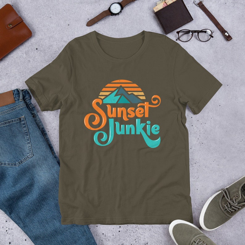 May include: A dark green t-shirt with a retro-style graphic of a mountain range with a sunset behind it. The text "Sunset Junkie" is written in a stylized font.