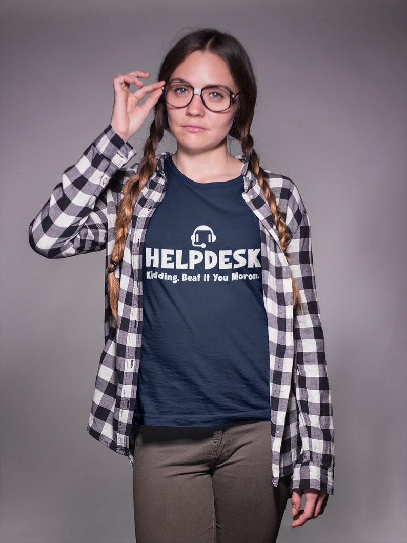 K&ouml;nnte beinhalten: Eine Frau tr&auml;gt ein marineblaues T-Shirt mit einer wei&szlig;en Grafik eines Headsets und dem Text "Helpdesk Kidding. Beat if You Moron." Sie tr&auml;gt auch ein schwarz-wei&szlig; kariertes Hemd und eine braune Hose.