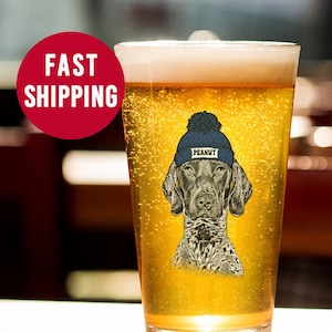 May include: A clear glass beer mug with a graphic of a dog wearing a blue beanie with the word "Peanut" on it. The dog is a German Shorthaired Pointer.